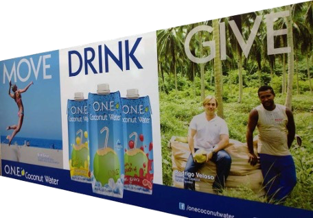 O.N.E. Coconut Water billboard reading Move, Drink and Give, with Rodrigo Veloso seated in a coconut grove